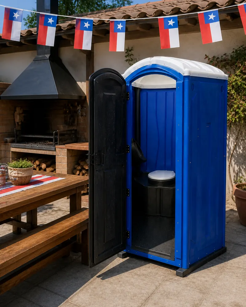 Baño químico azul junto a un quincho con banderines chilenos, listo para un asado del 18