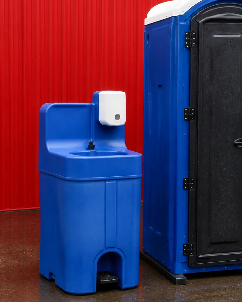 Lavamanos portátil azul con dispensador de jabón junto al baño químico